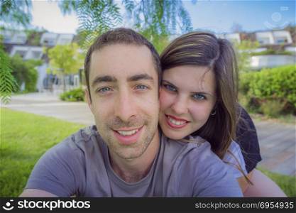 Happy couple taking selfie with smartphone or camera in the park.