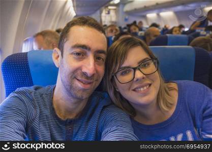 Happy couple taking selfie with smartphone or camera inside airplane.