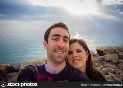 Happy couple taking selfie with smartphone or camera over sunset coast background.