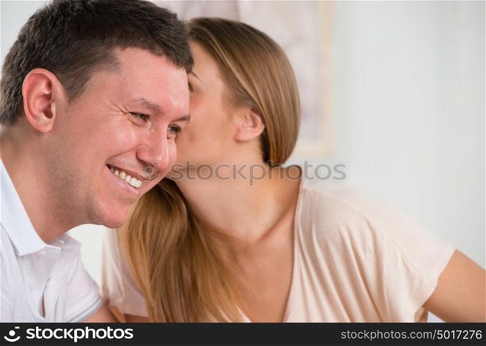 Happy couple talking and gossiping in their living room, woman whispering something to her husband
