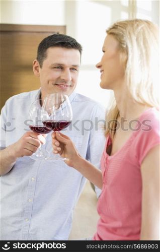 Happy couple toasting red wine glasses in kitchen