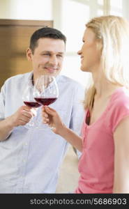 Happy couple toasting red wine glasses in kitchen