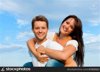 Happy couple under a blue sky; he is carrying her piggyback