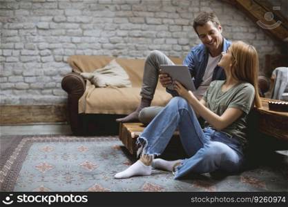 Happy couple using digital tablet while sitting  together oh the floor in the room
