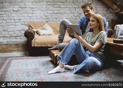 Happy couple using digital tablet while sitting  together oh the floor in the room