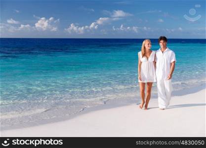 Happy couple walking along beautiful sandy beach, young family holding hands and enjoying honeymoon vacation on Maldives