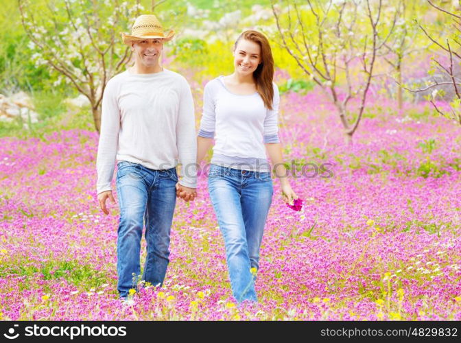 Happy couple walking outdoors, beautiful spring garden, pink floral field, romantic date, love concept