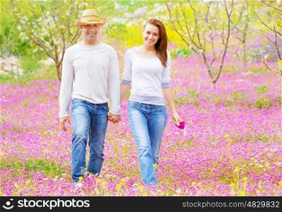 Happy couple walking outdoors, beautiful spring garden, pink floral field, romantic date, love concept