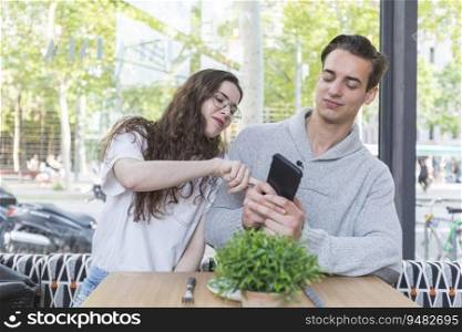 Happy couple watching mobile at winery bar - Woman and man sitting outside while smiling looking at smartphone - Lifestyle and tech concept