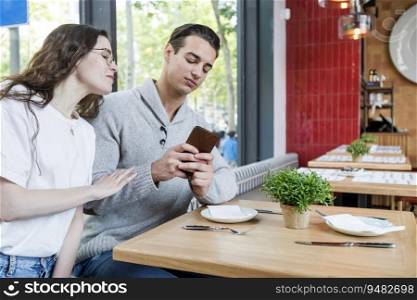 Happy couple watching mobile at winery bar - Woman and man sitting outside while smiling looking at smartphone - Lifestyle and tech concept