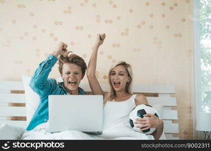 Happy couple watching soccer football on the bed