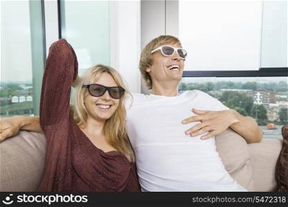 Happy couple wearing 3D glasses while sitting on sofa at home