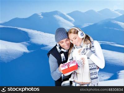 Happy couple with gift, people outdoor at winter snow mountains, young man giving present to beautiful woman, Christmas vacation holidays, love concept