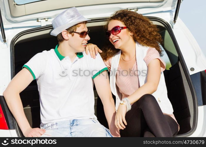 Happy couple. Young happy couple sitting in car trunk outdoor