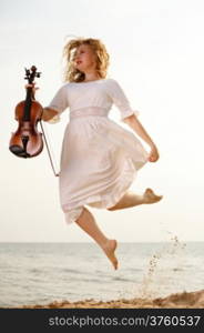 Happy crazy blonde girl music lover on beach jumping with a violin. Love of music concept.