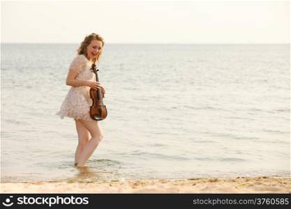 Happy crazy blonde girl music lover on beach with a violin. Love of music concept.