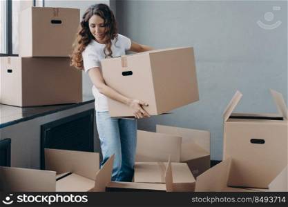 Happy curly girl carrying box and relocating. Hispanic woman unpacking boxes. Attractive girl is new home owner. Real estate and property advertising mockup concept.. Happy curly girl carrying box and relocating. Real estate and property advertising mockup concept.