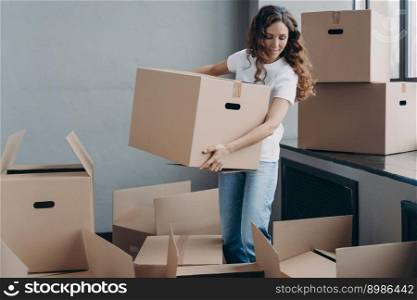 Happy curly girl carrying box and relocating. Hispanic woman unpacking boxes. Attractive girl is new home owner. Real estate and property advertising mockup concept.. Happy curly girl carrying box and relocating. Real estate and property advertising mockup concept.