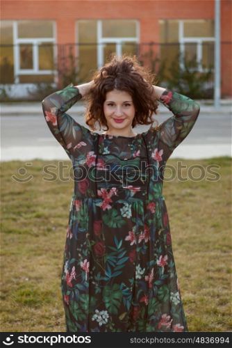 Happy curvy girl with curly hair in the street with a flowered dress touching her hair