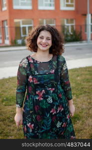 Happy curvy girl with curly hair in the street with a flowered dress and closed eyes