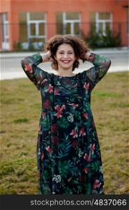Happy curvy girl with curly hair in the street with a flowered dress touching her hair