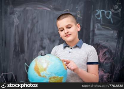 happy cute boy learning about the world using globe of earth while standing in front of black chalkboard