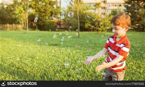 Happy cute boy playing to catch soap bubbles in the park. Happy boy playing with soap bubbles in the park