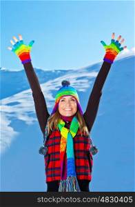 Happy cute girl playing in snow outdoor, looking up with hands up, beautiful woman smiling with raised arms to blue sky and nature, young teen female wearing colorful hat, Christmas winter holidays travel and vacation