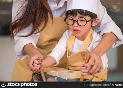 Happy cute little boy with eyeglasses and beautiful Asian mother prepare to cooking in kitchen at home. People lifestyles and Family. Homemade food and ingredients concept. Two Thai people life
