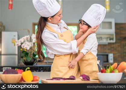 Happy cute little boy with eyeglasses looking beautiful Asian woman mother each other while prepare to cooking in kitchen at home. People lifestyles and Family. Homemade food and ingredients concept.