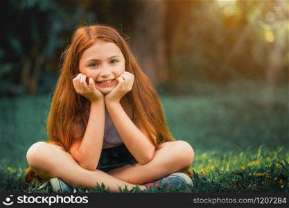 Happy cute little girl playing in the outdoor park in summer. Child expression and lifestyle.. Happy cute little girl sitting in the park.