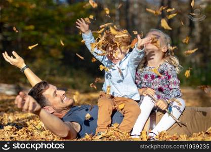 Happy dad and children playing with autumn leaves in forest