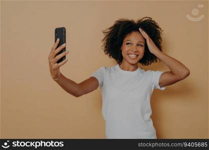 Happy dark-skinned woman in white shirt, taking a cheerful selfie with a modern smartphone.