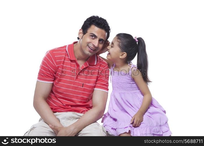 Happy daughter whispering in father&rsquo;s ear over white background