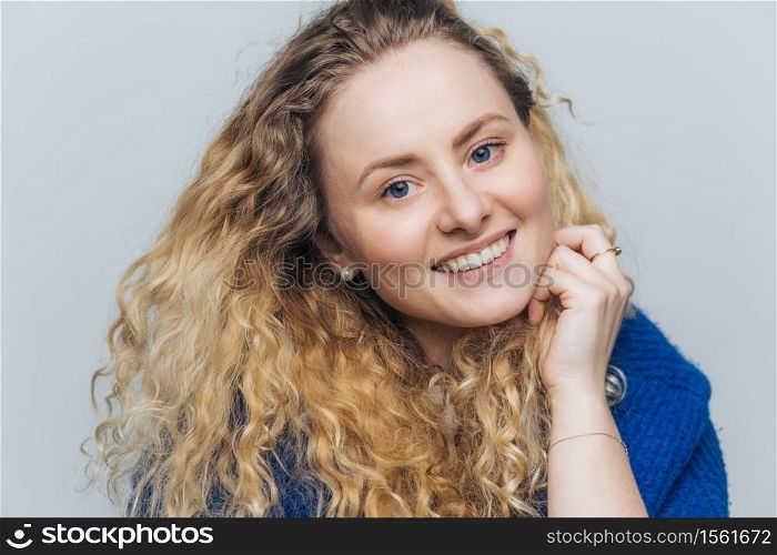 Happy delighted female student with broad smile, laughs pleasantly at camera, rejoices successfully passed exams, has long holidays, isolated over blue studio background. Positive emotions concept