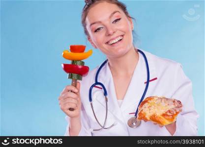 Happy dietitian nutritionist with sweet roll bun and vegetables like cucumber, tomato and pepper. Woman holding comparing junk and healthy food. Right eating nutrition concept.