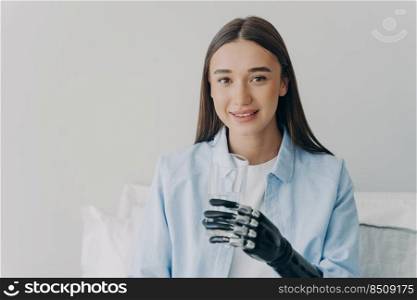 Happy disabled girl grasps a glass with myoelectric hand. High technology prosthesis. Nervous control sensored hand. European woman is smiling. Technology and science innovation concept.. Disabled girl grasps a glass with myoelectric hand. High technology prosthesis.