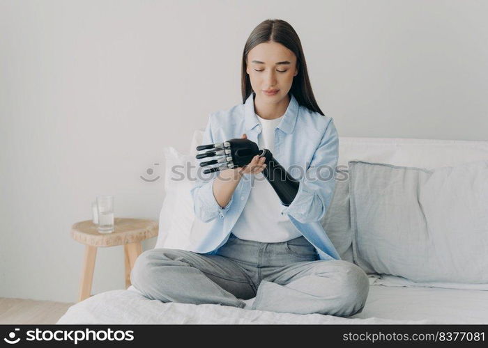 Happy disabled woman is assembling electronic control prosthesis and setting functions with processor chip. European girl adjusting her artificial arm. Innovation for daily routine of the handicapped.. Disabled young woman is assembling electronic control prosthesis. Artificial arm adjusting.