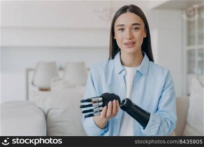 Happy disabled young woman is assembling bionic limb prosthesis. Attractive caucasian girl has cyber sensor hand. Female&utee setting her myoelectric arm at home. Innovations in medicine.. Happy disabled young woman is assembling bionic limb prosthesis. Attractive girl has cyber hand.