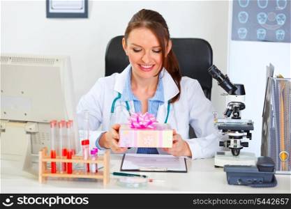 Happy doctor woman sitting in cabinet with present in hands&#xA;