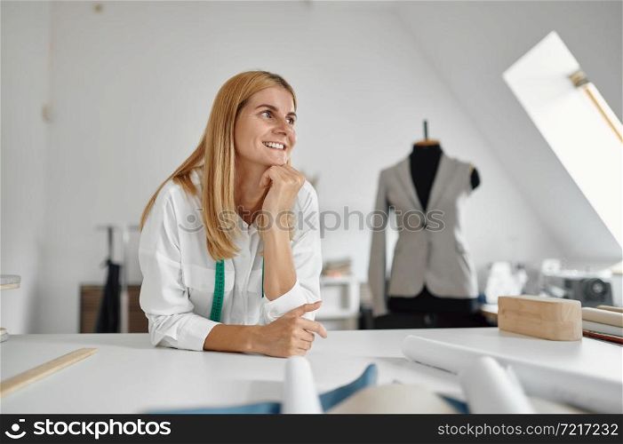 Happy dressmaker poses at her workplace in workshop. Dressmaking occupation and professional sewing, handmade tailoring business, handicraft hobby. Happy dressmaker poses at workplace in workshop