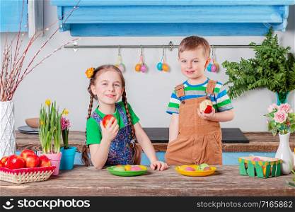 Happy easter. Cute brother and sister eat apples in the kitchen, cheerful children, a boy and a girl are preparing for the holiday. Easter decoration.. Happy easter. Cute brother and sister, funny kids boy and girl are preparing for the holiday.