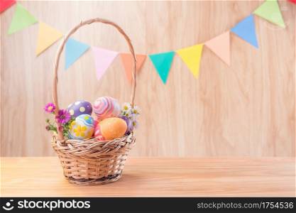 Happy Easter day colorful eggs and flowers in the basket on wooden floor have blurred celebrate banner party flags with copy space.