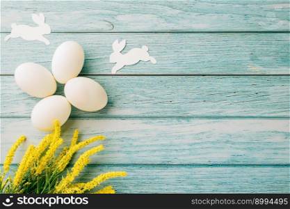Happy Easter Day Concept. Flat lay of holiday banner background design white easter eggs and beautiful yellow flowers on blue wooden background with empty copy space, celebration greeting card