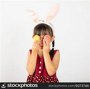 Happy Easter Day. Smi≤Asian litt≤girl wearing easter bunny ears holding colorfull eggs closes eyes with testic≤s isolated on white background with©space, Happyχld in holiday