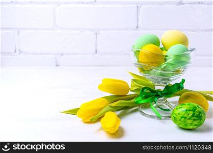 Happy Easter greeting background with green and yellow painted eggs in the glass vase and tulips, copy space