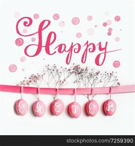 Happy Easter greeting card lettering with hanging pastel pink Easter eggs on ribbon with flowers at white wall background