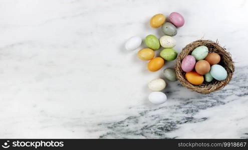 Happy Easter holiday concept with basket of colorful eggs and nest on stone background in flat lay format 