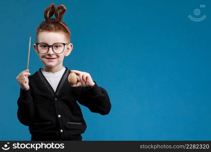 Happy Easter kids. Boy in rabbit bunny ears on head painting easter egg with paintbrush on blue background. Cheerful smiling child in glasses.. Happy Easter kids. Boy in rabbit bunny ears on head painting easter egg with paintbrush on blue background. Cheerful smiling child in glasses