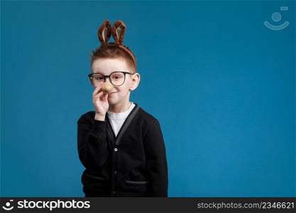 Happy Easter kids. Boy in rabbit bunny ears on head with colored egg on blue background. Cheerful smiling child in glasses.. Happy Easter kids. Boy in rabbit bunny ears on head with colored egg on blue background. Cheerful smiling child in glasses